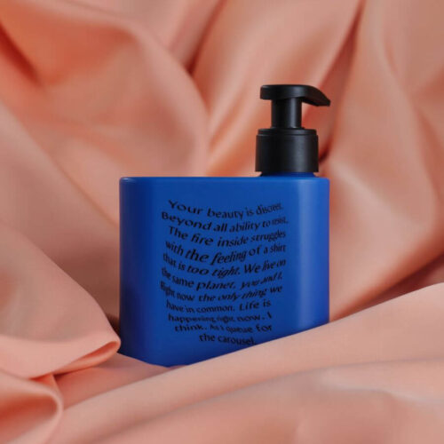 Blå flaska med Meyenberg Bergamot and Sea Salt handtvål på rosa tygbakgrund.