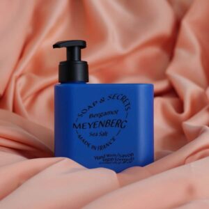 Blå flaska med Meyenberg Bergamot and Sea Salt handtvål på rosa tygbakgrund.